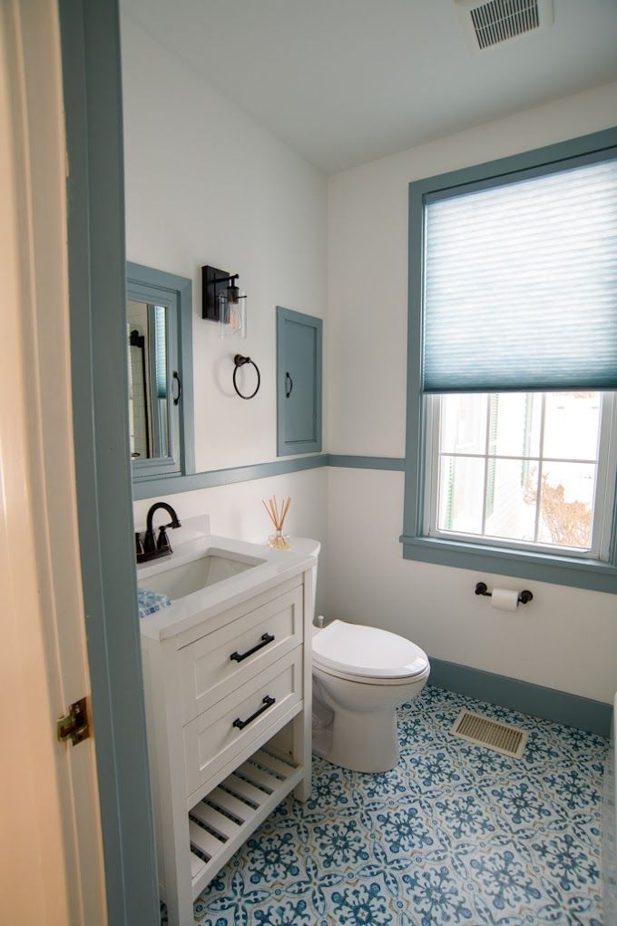 Small bathroom with blue trim, patterned blue tile floor, white vanity, toilet, and window blinds.