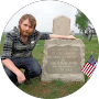 Person kneeling beside a gravestone in a cemetery, holding a small American flag.