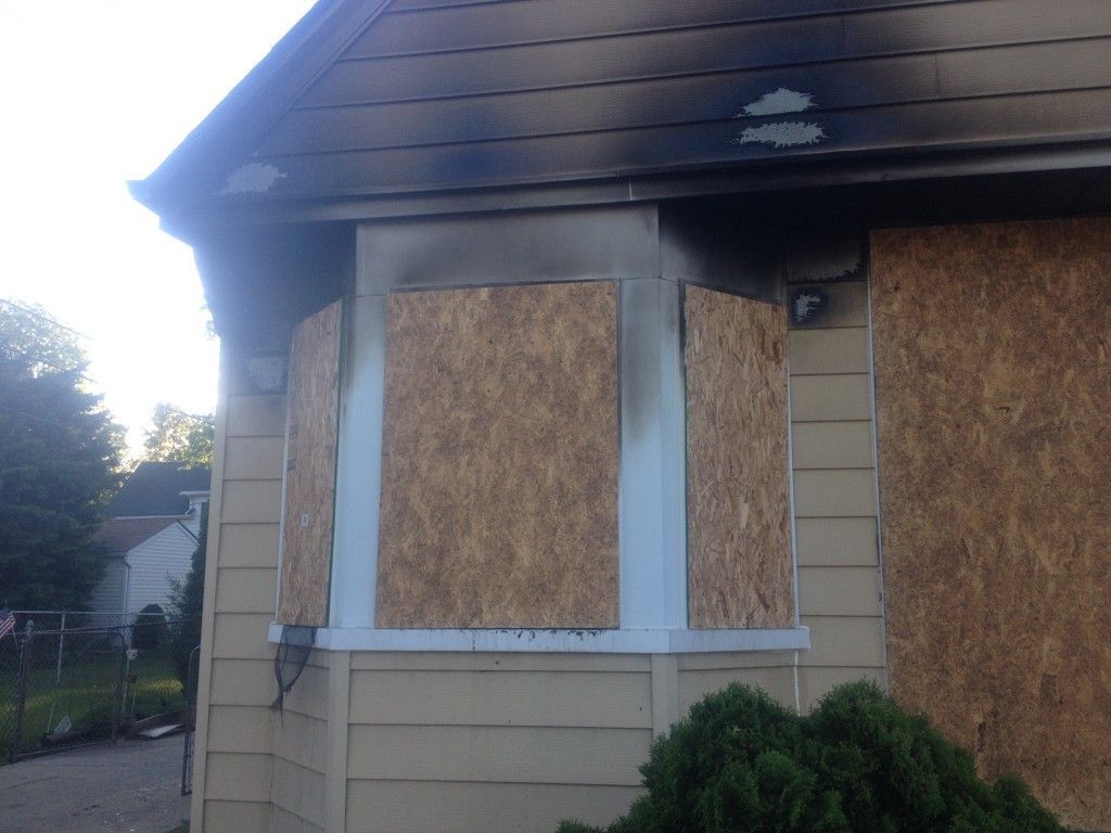 Boarded-up house exterior with plywood-covered windows and beige siding