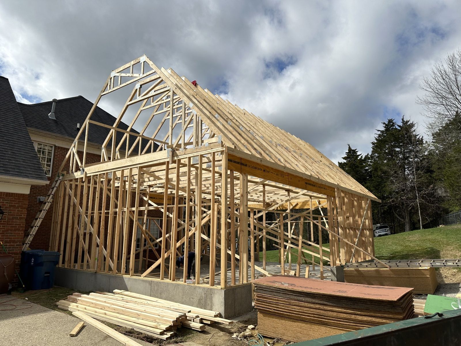 Wood-frame house under construction with exposed trusses and lumber on a foundation