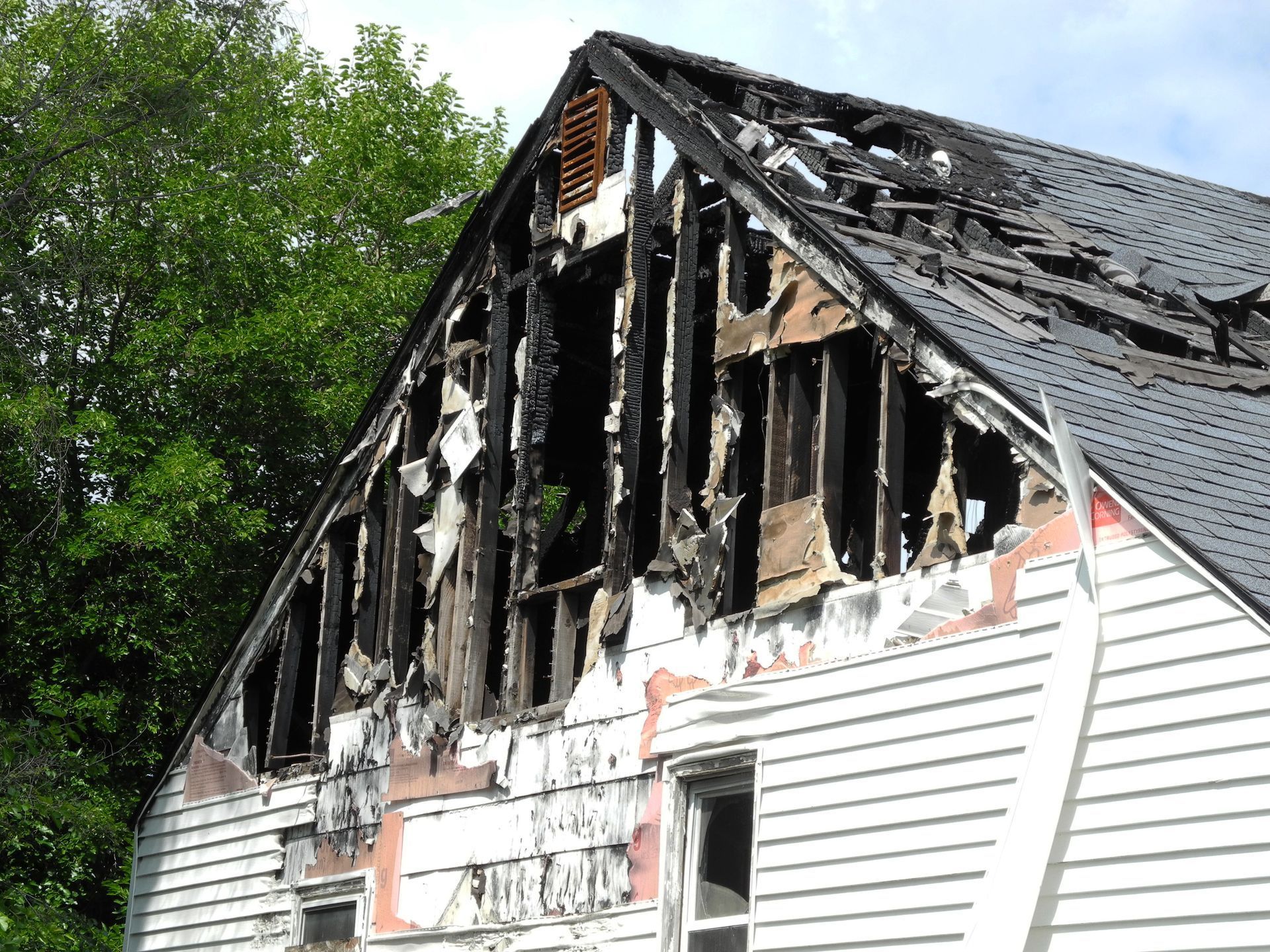 Charred house exterior with burned roof and damaged white siding after a fire