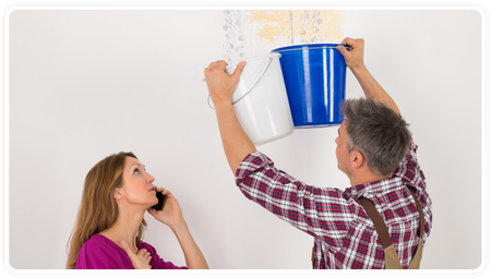 Man and woman inspecting a water leak on a wall, with blue and white buckets catching drips.