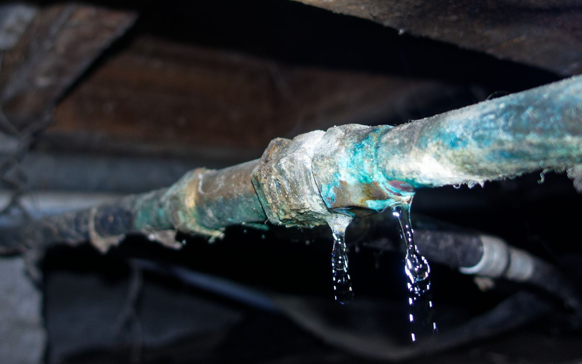 Leaking corroded pipe with water dripping in a dark crawl space