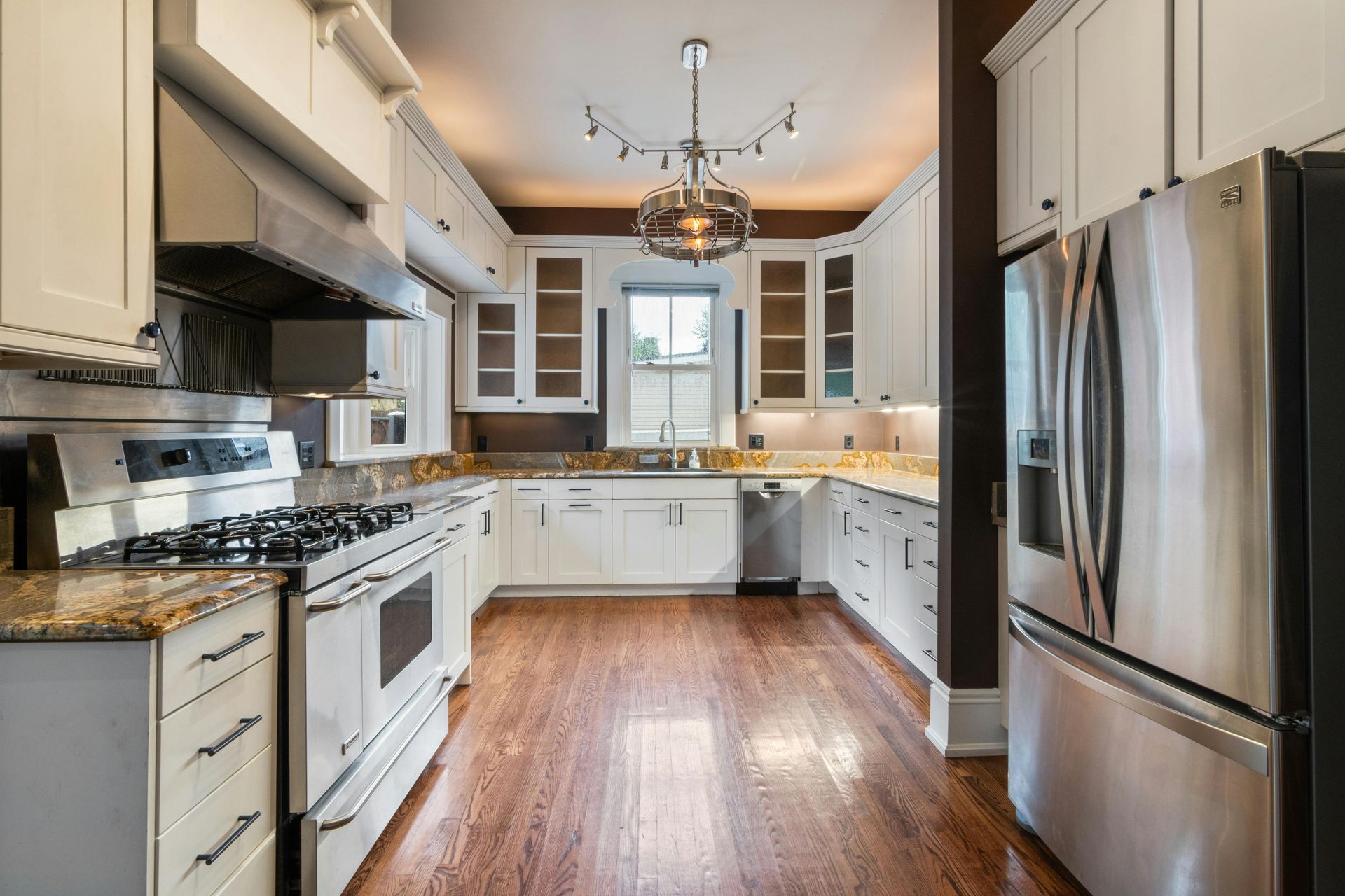 Bright kitchen with white cabinets, stainless steel appliances, wood floors, and a chandelier.