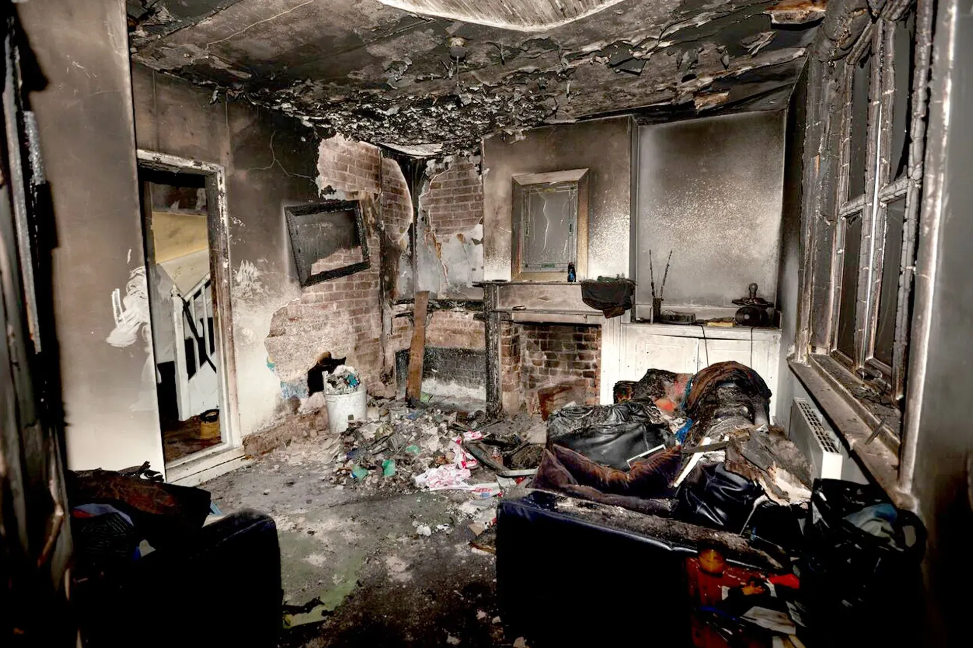 Burned, smoke-damaged living room with debris scattered across the floor and charred walls