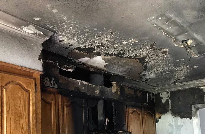 Fire-damaged kitchen ceiling and upper cabinets with heavy soot and charring
