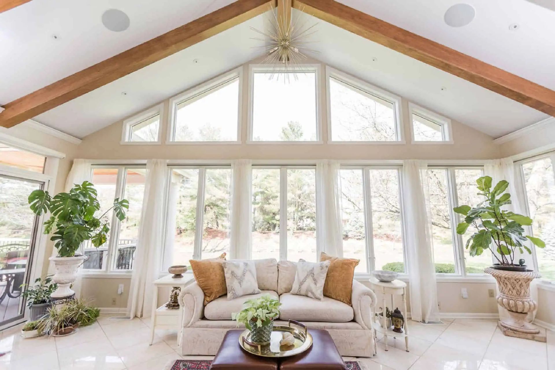 Bright sunroom with vaulted ceiling, large windows, white sofa, and potted plants