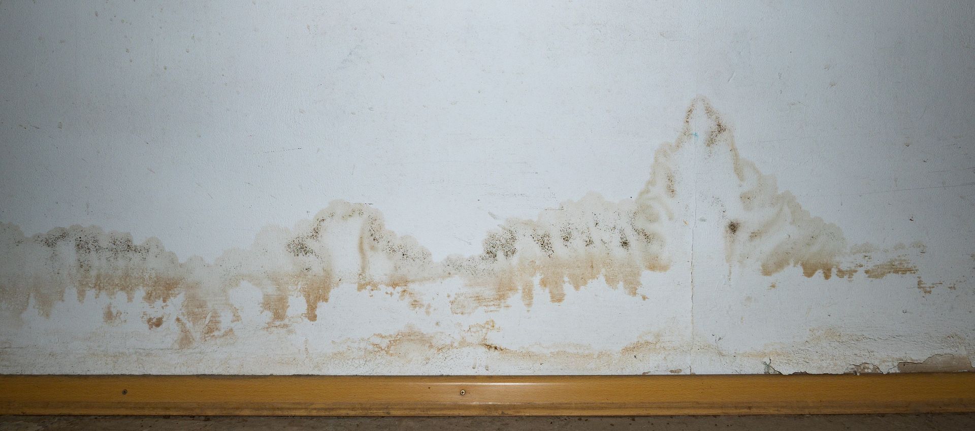 Peeling and water-damaged white wall above a wooden baseboard.