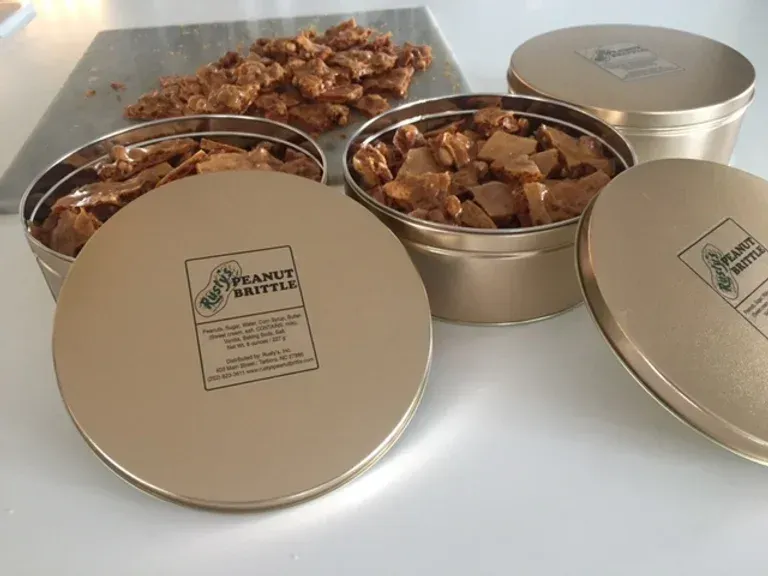 Three tins of peanut brittle are stacked on top of each other