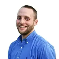 A man with a beard is wearing a blue shirt and smiling.