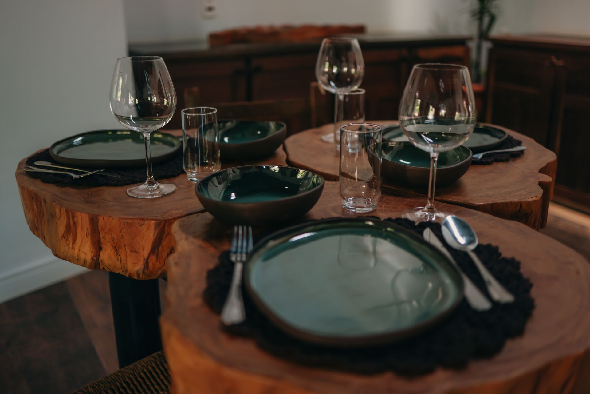 Mesa posta para uma refeição, incluindo pratos, tigelas, talheres e taças de vinho, sobre uma mesa feita com um tronco de árvore.