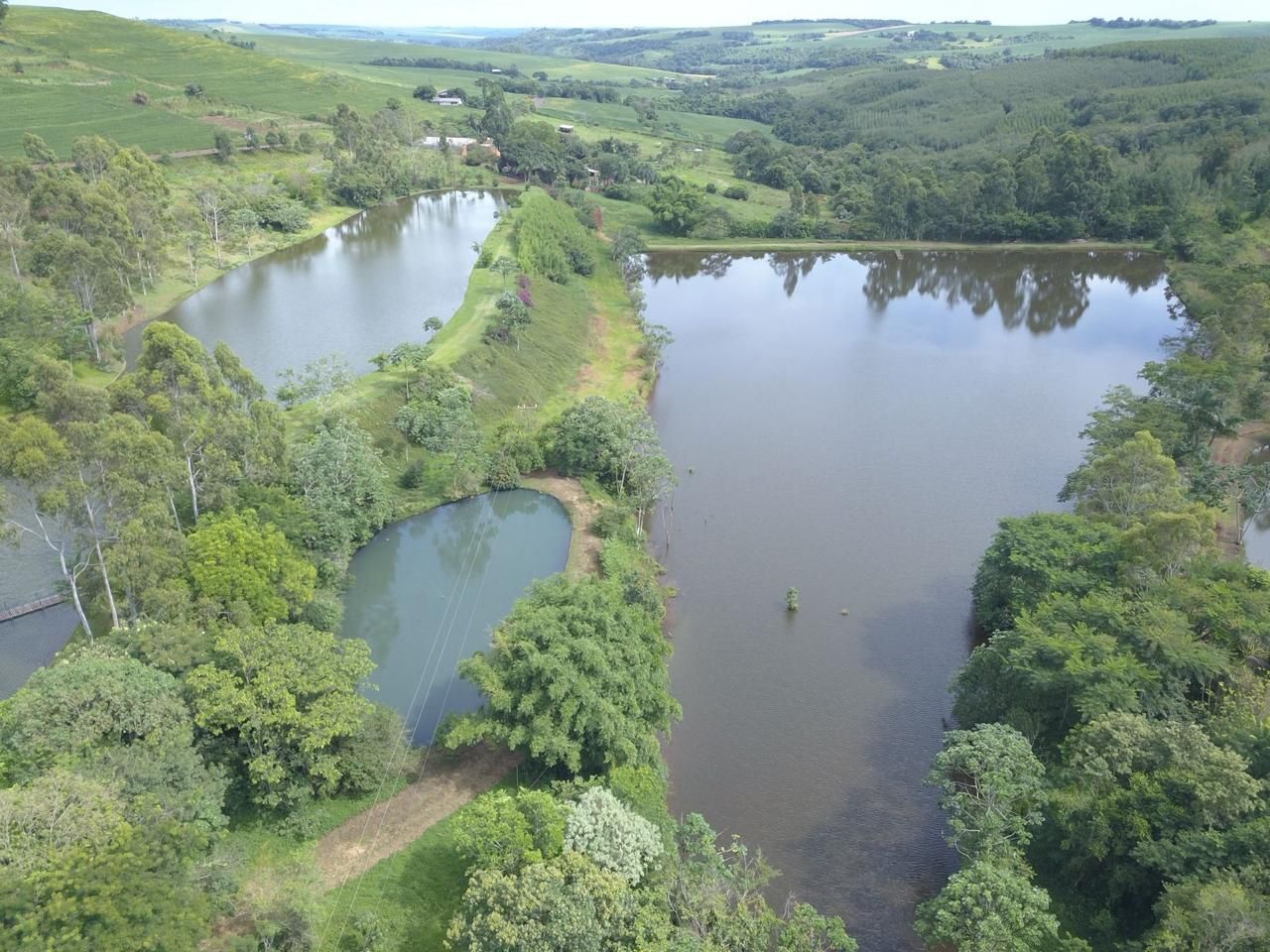 Vista aérea de três lagos interligados, rodeados por árvores verdes e colinas.