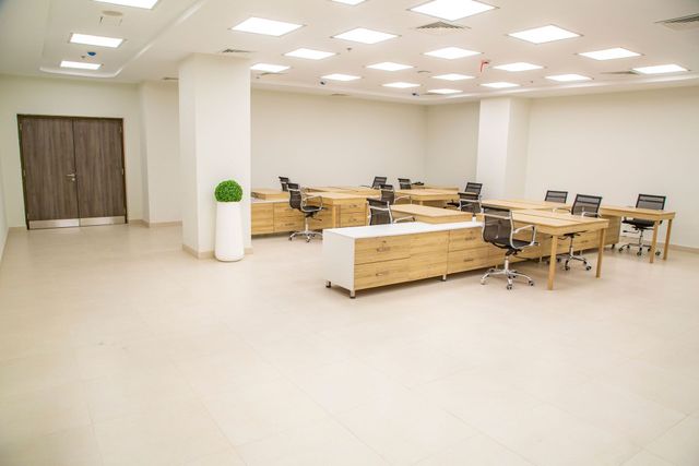 Bright office workspace with cubicles, desks, and a few people working under fluorescent ceiling lights