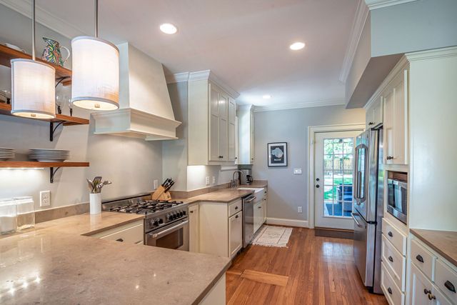Bright modern kitchen with white cabinets, marble counters, wood floors, and stainless-steel appliances