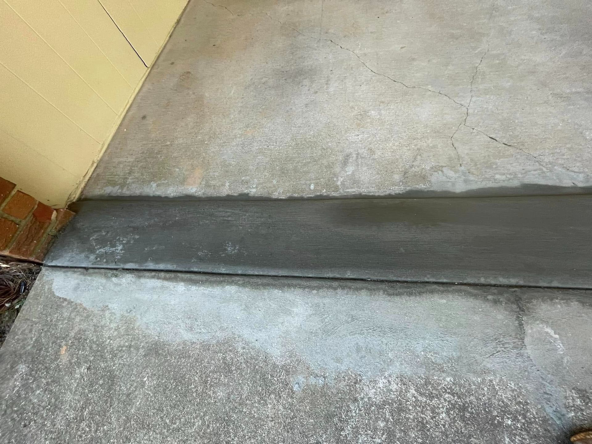 Concrete walkway with a dark gray expansion joint beside a beige wall and curb.