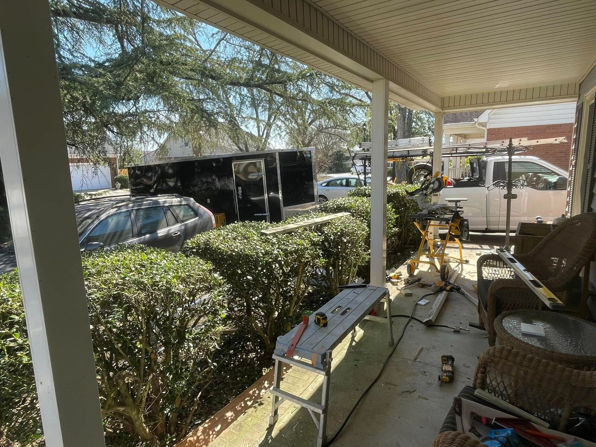 Porch with white columns, wicker chairs, hedge, parked car, and a small table in the foreground