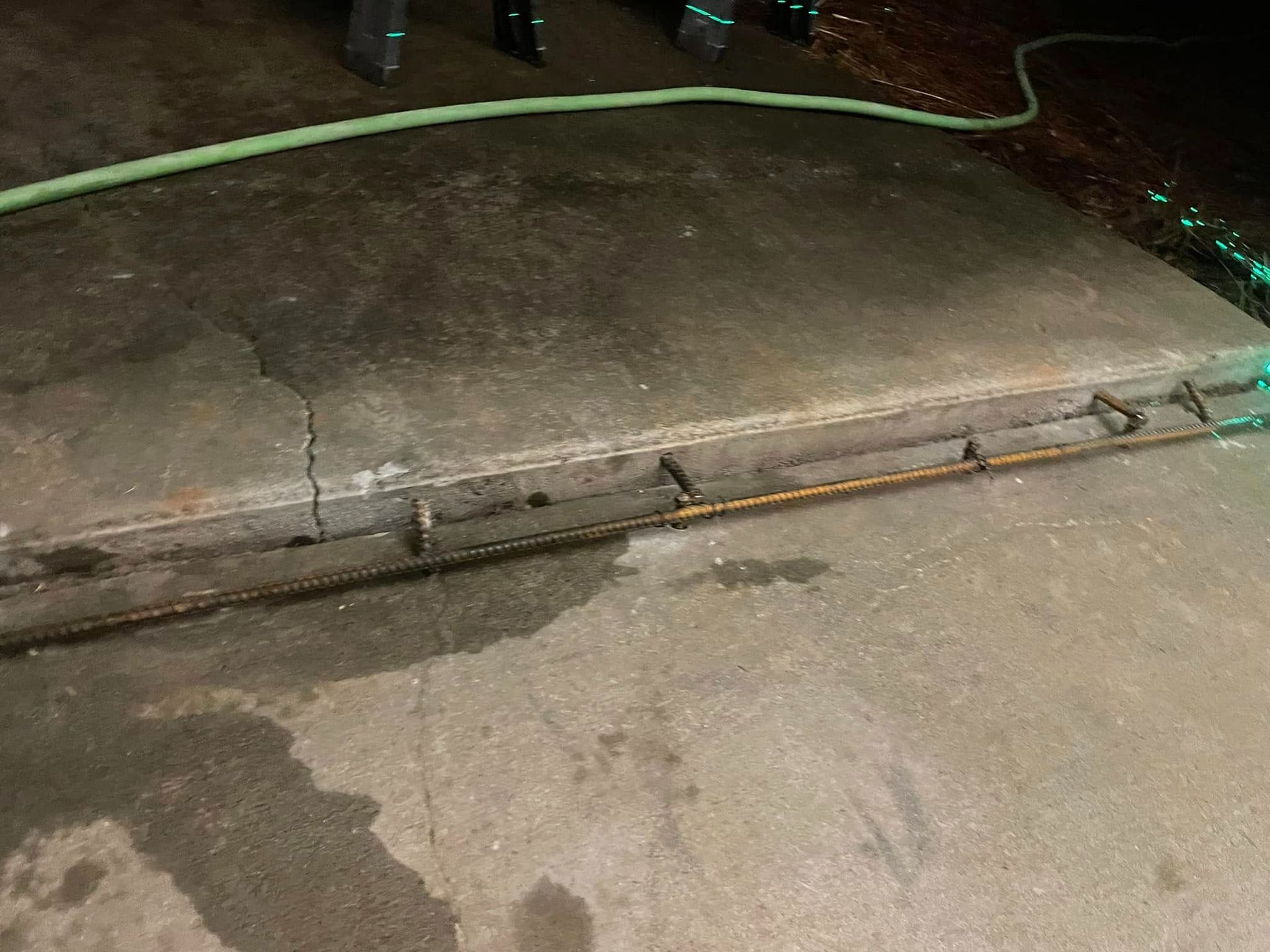 Wet concrete sidewalk with a green hose and a curb at night
