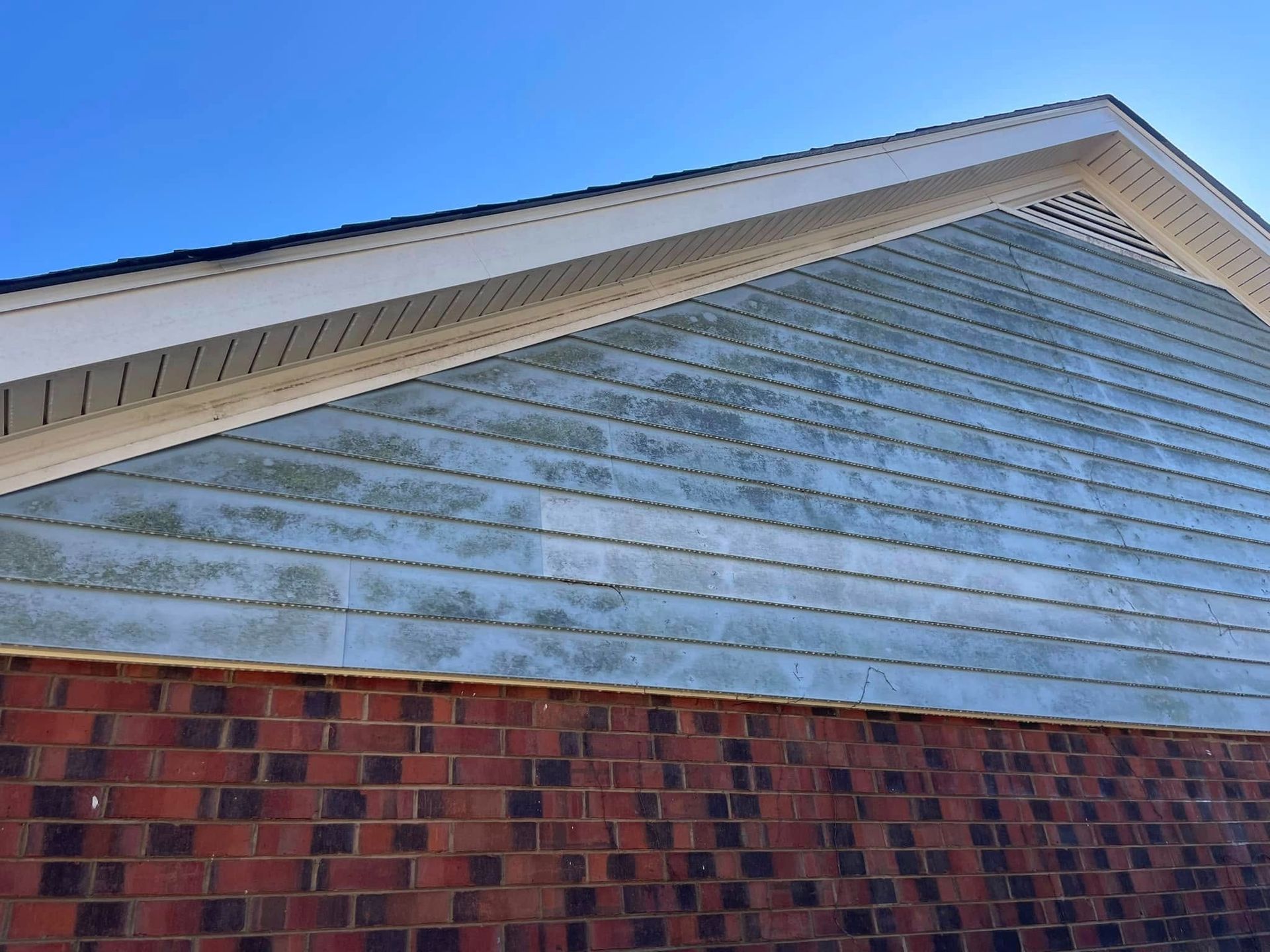 House gable with white siding above red brick under a blue sky