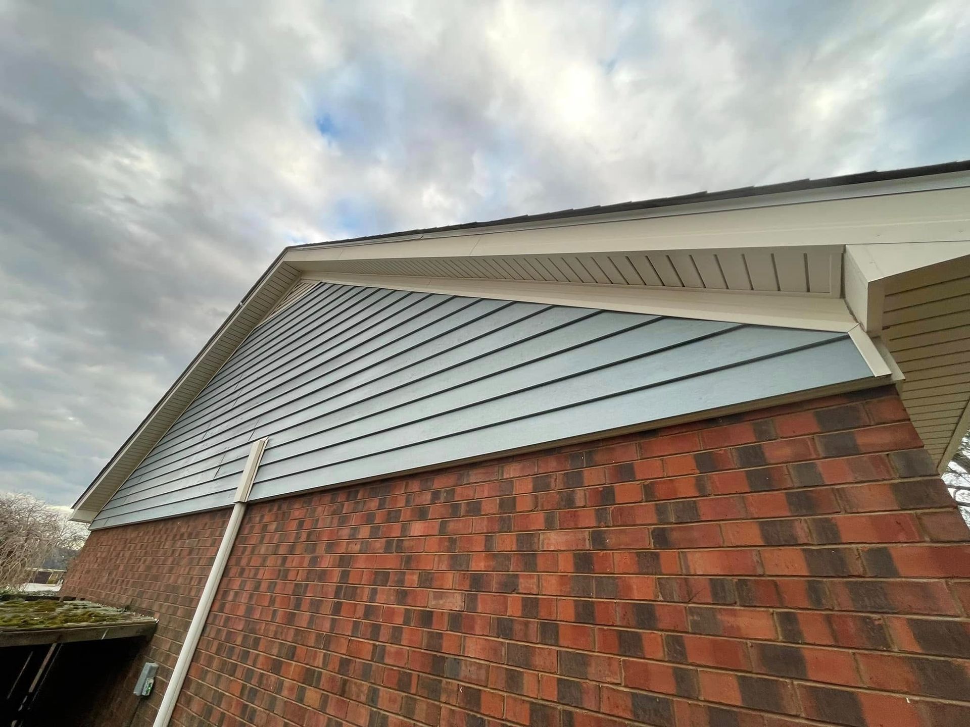 Exterior of a house with brick walls, white siding, and a cloudy sky overhead
