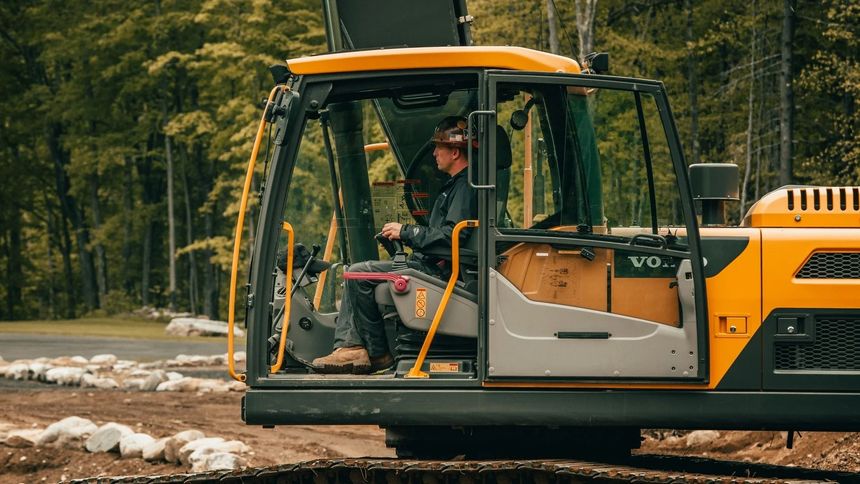 Yellow excavator clearing muddy ground in a forest, with an operator in the cab