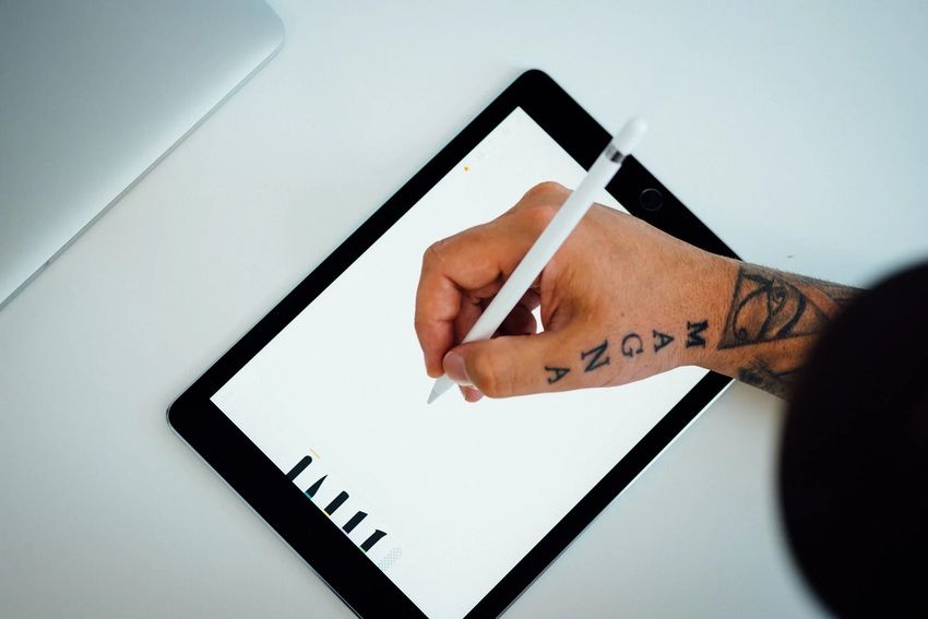 Hand holding a stylus over a tablet, sketching on a blank white screen