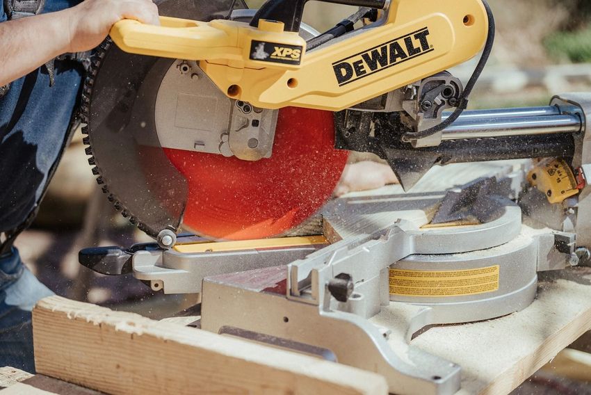 Yellow DeWalt miter saw cutting wood, with a red blade guard in a workshop.