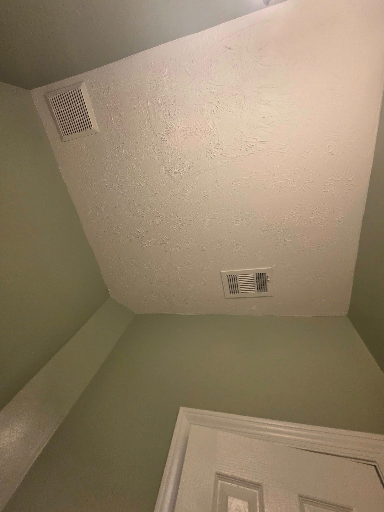 Ceiling corner of a room with vent and light fixture above a door.