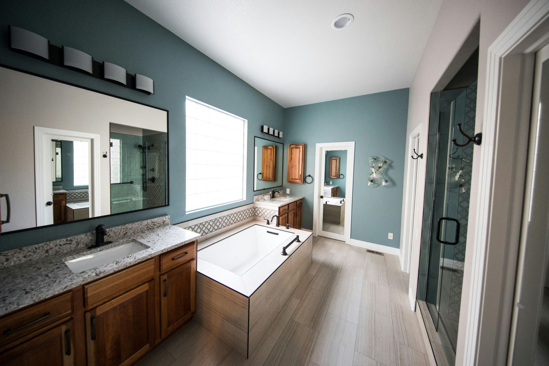 Bright bathroom with double vanity, large mirror, freestanding tub, and teal walls