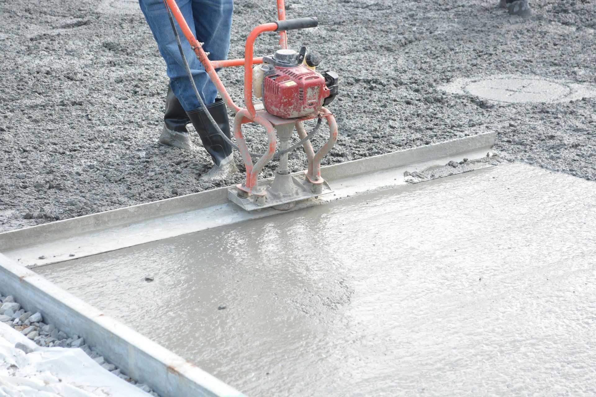 Worker using a power trowel to smooth wet concrete on a slab outdoors