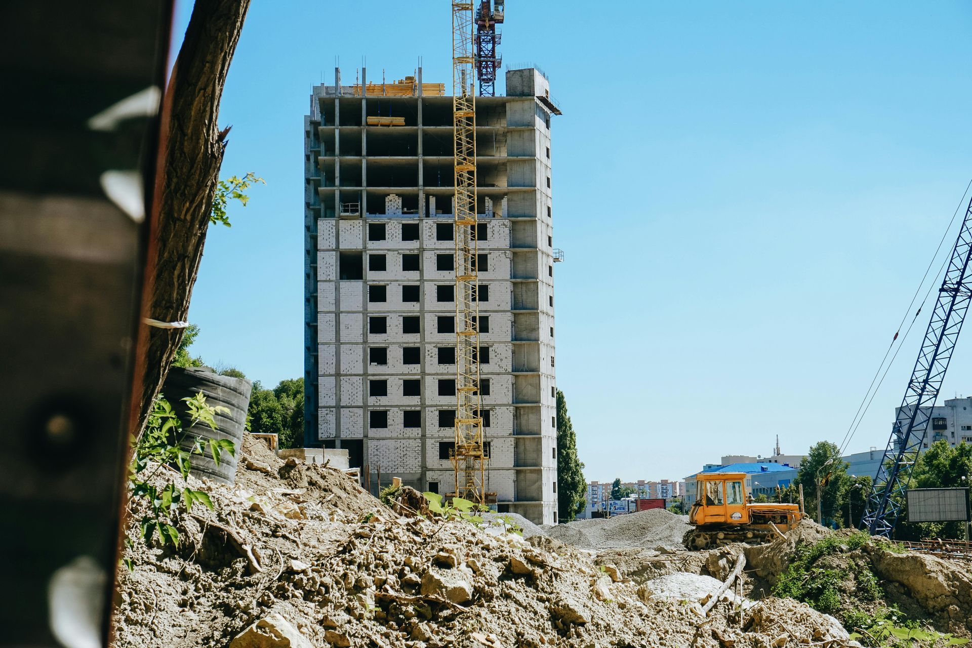 Partially built high-rise with a crane, rubble in foreground, and construction vehicles on site