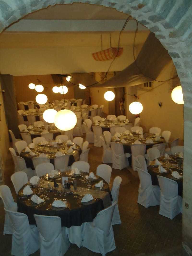 Binnenruimte voor evenementen met ronde tafels voor een formeel diner. Witte tafellakens en stoelhoezen zijn zichtbaar onder zacht licht.