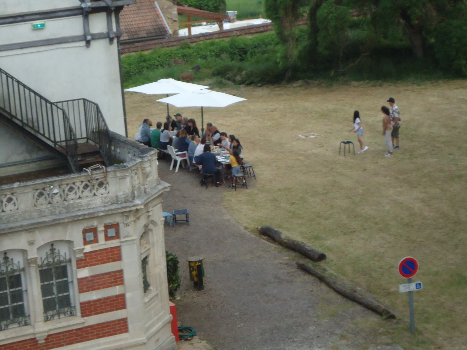 Een groep mensen zit aan tafels onder parasols in een park