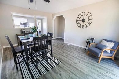 Dining room with black table and chairs, wall clock, and blue armchair on wood-look flooring.