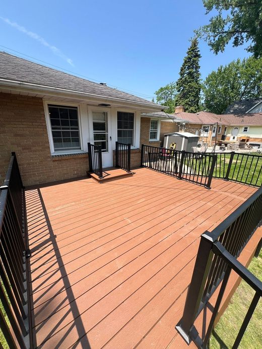 Spacious red deck with black railings beside a brick house, under a bright blue sky.