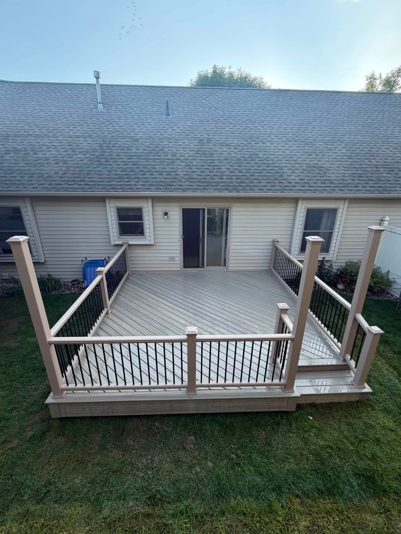 Raised wooden deck with white railing in a backyard behind a house with sliding glass doors.