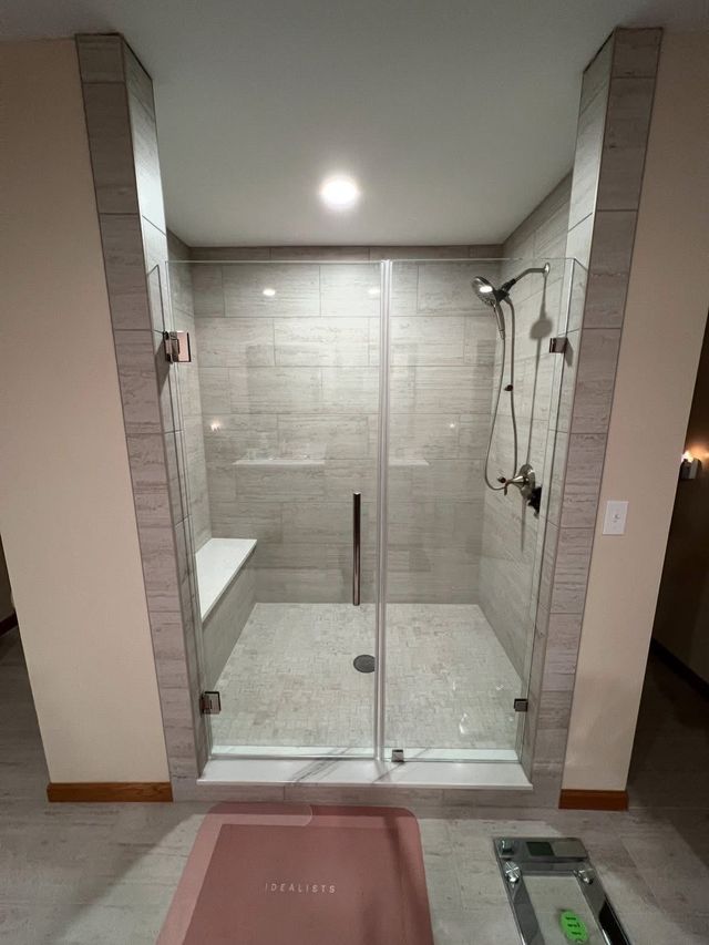 Glass-enclosed walk-in shower with beige tile, built-in bench, and handheld showerhead.