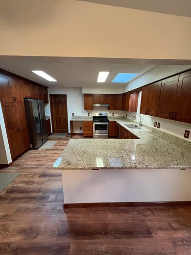 Empty modern kitchen with wood cabinets, granite island, stainless fridge, and skylight lighting