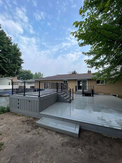 Outdoor patio with metal railings, steps, and tables under trees beside a building.
