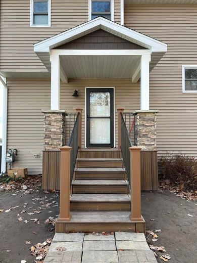 Front porch entrance with white posts, stone columns, wooden stairs, and a glass storm door.