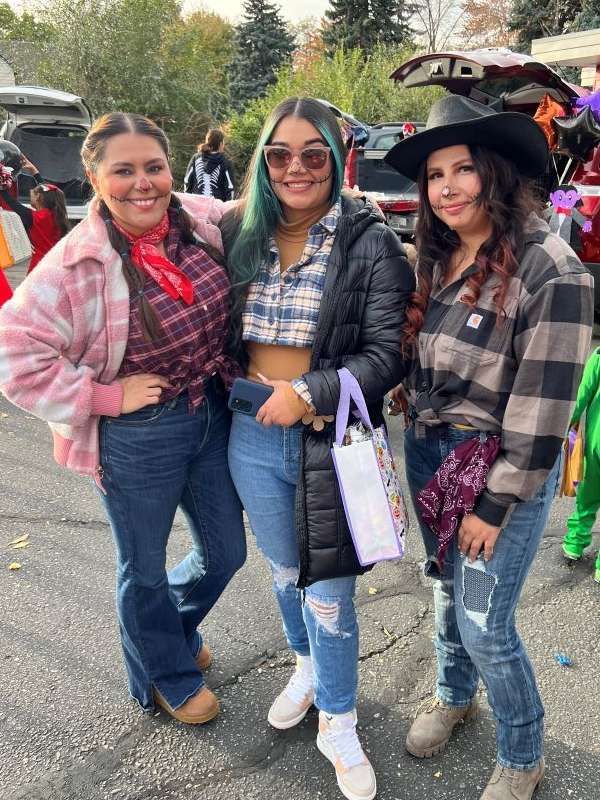 Three women are posing for a picture at a trunk or treat event.