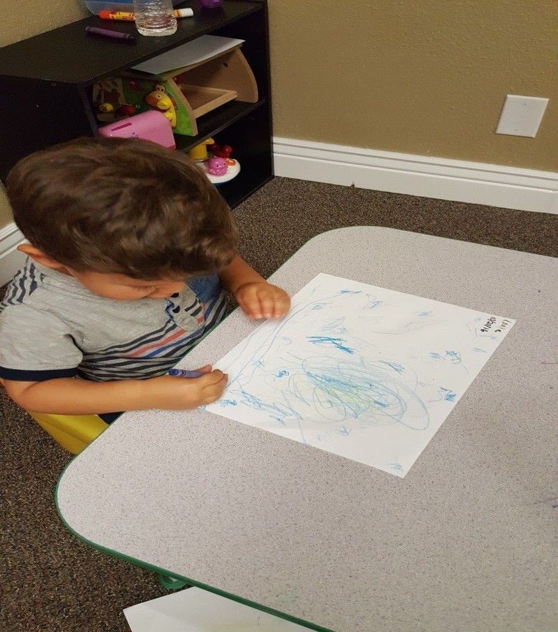 A young boy is sitting at a table drawing on a piece of paper