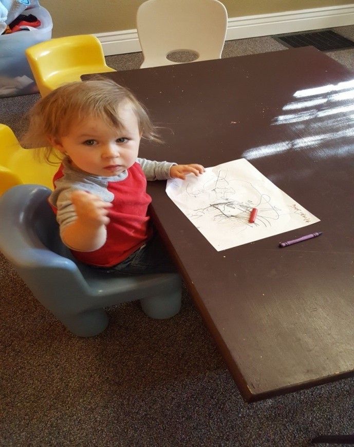 A little girl is sitting at a table with a drawing on it