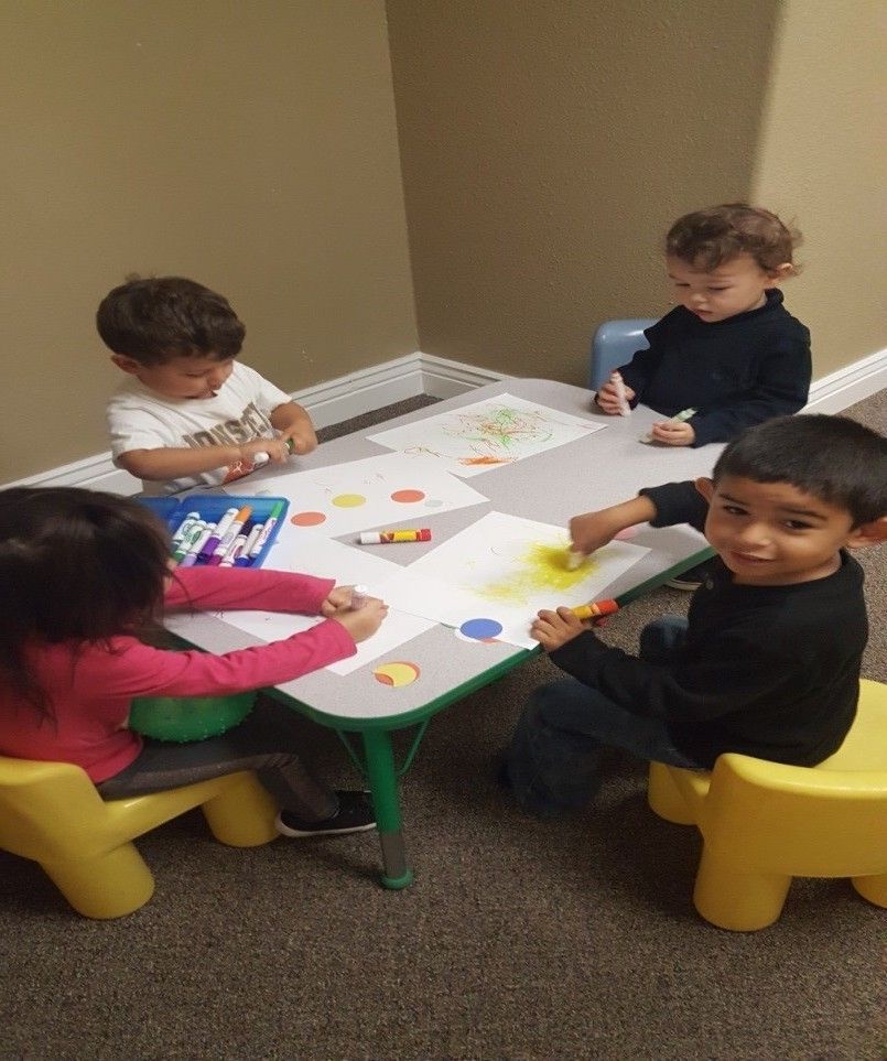 A group of children are sitting at a table drawing with markers.