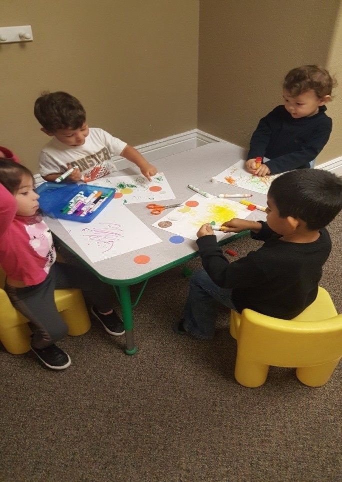 A group of children are sitting around a table playing with markers.