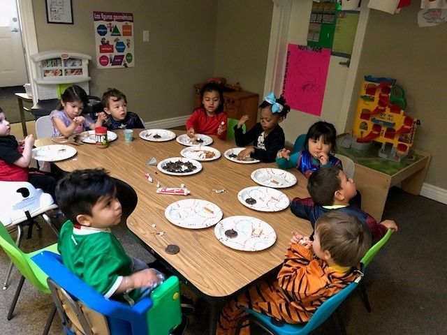 A group of children are sitting around a table with plates of food.