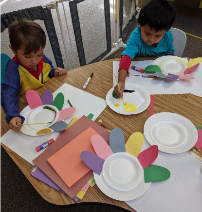 Two young boys are sitting at a table playing with paper flowers