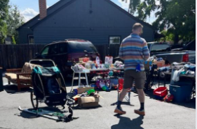 A yard sale set up in a driveway; a man walks toward items for sale.