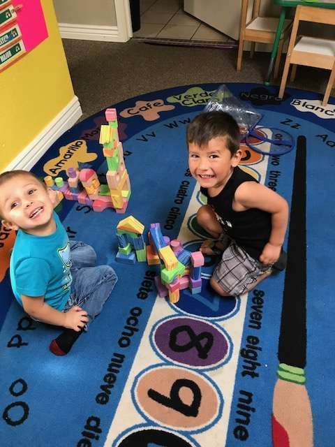 Two young boys are playing with blocks on a rug that says seven eight nine