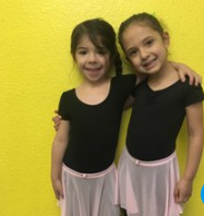 Two little girls are standing next to each other in front of a yellow wall.
