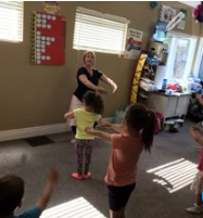 A woman is teaching a group of children how to dance in a room.